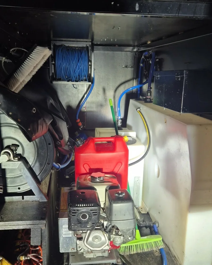 The pressure cleaning unit inside the truck body: petrol driven pump, hose reel, brushes and a fuel can.
